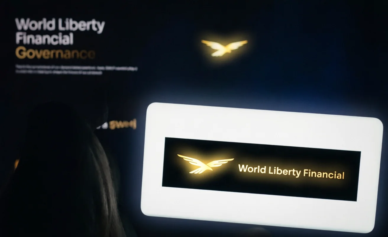 World Liberty Financial logo displayed on a screen in the foreground and projected in the background in a dark environment.