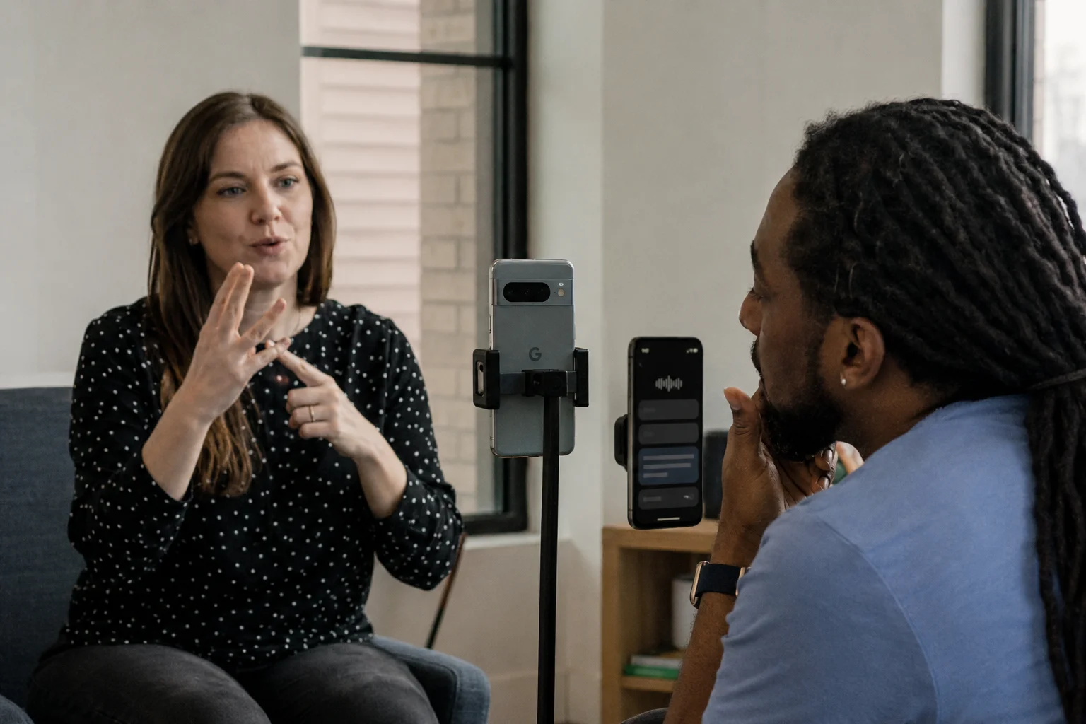 Woman uses sign language in front of a Pixel smartphone camera while another person follows the transcription displayed on the device.