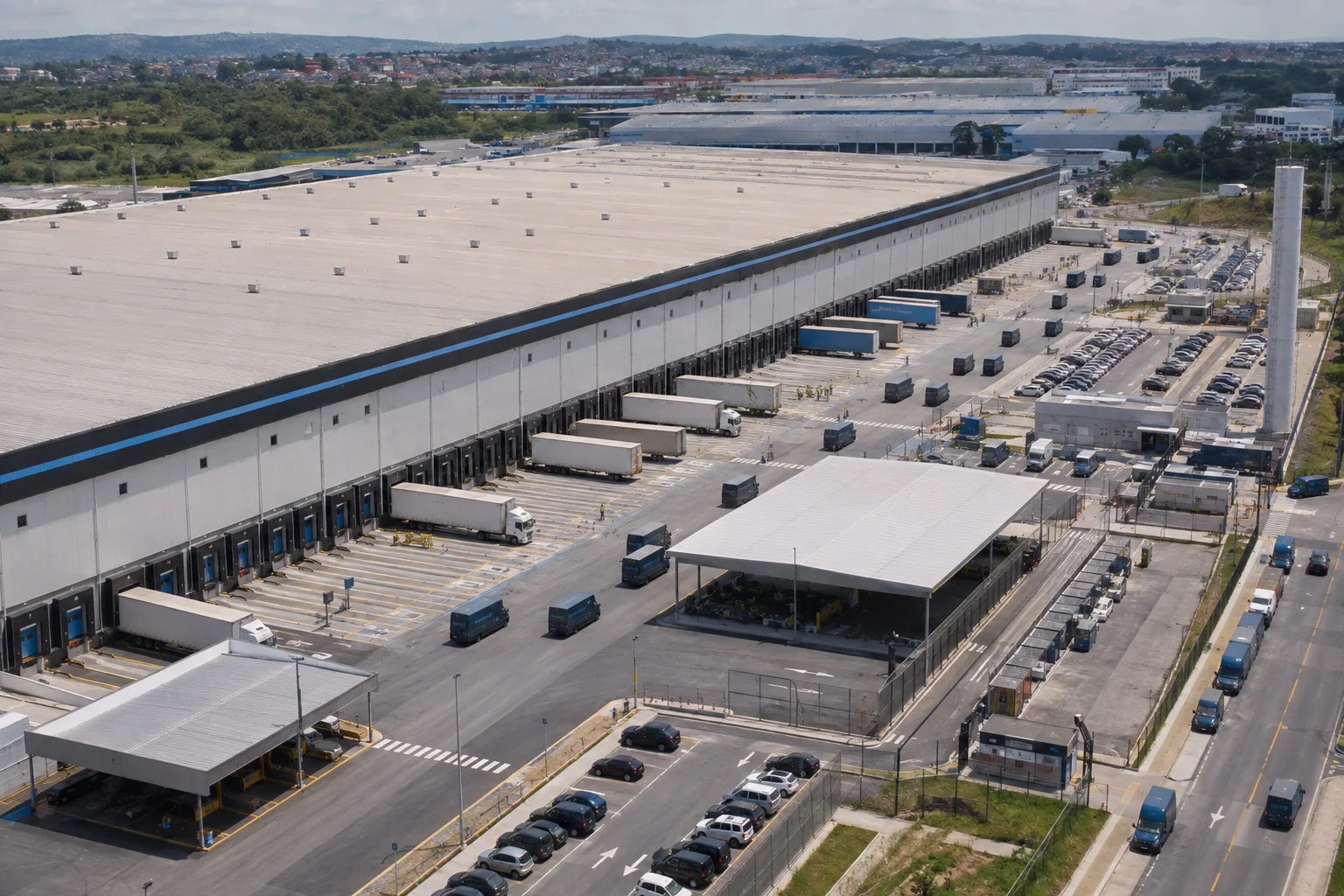 Aerial view of a large logistics center in operation, with trucks, delivery vans, loading docks and extensive distribution infrastructure in an urban area.