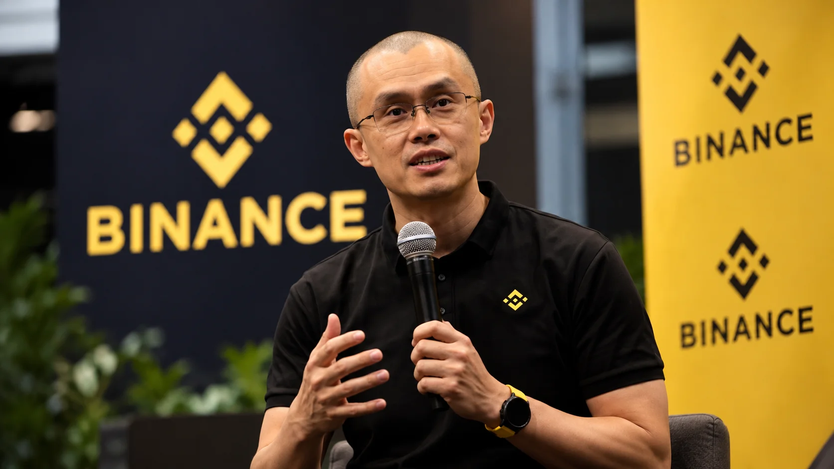 Fundador da Binance durante apresentação, com a identidade visual da empresa ao fundo.