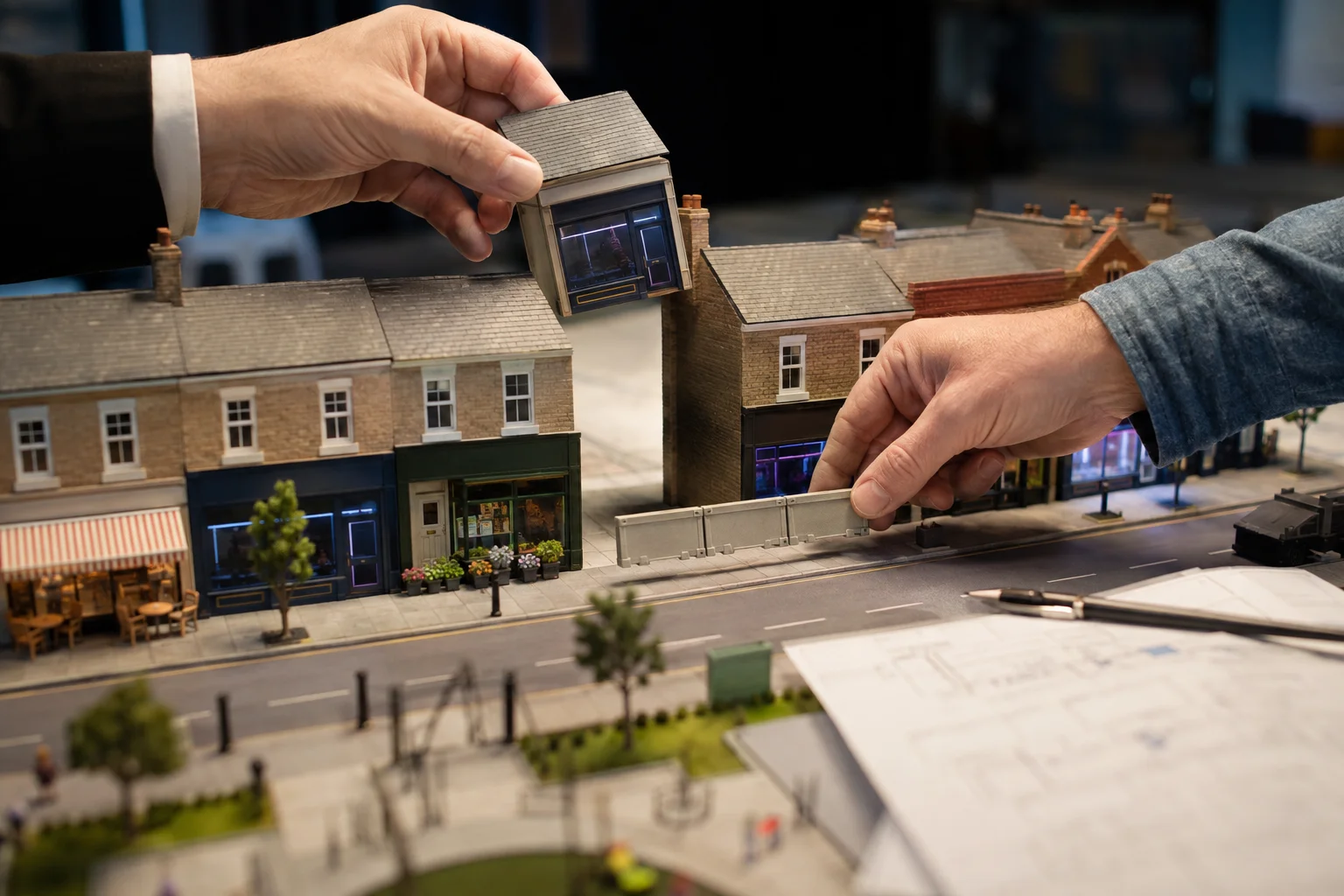 Duas mãos interagem sobre uma maquete de rua comercial britânica: uma posiciona a peça de uma nova casa de apostas sobre um imóvel vazio, enquanto a outra coloca uma barreira à frente do espaço, entre cafés, lojas e serviços.