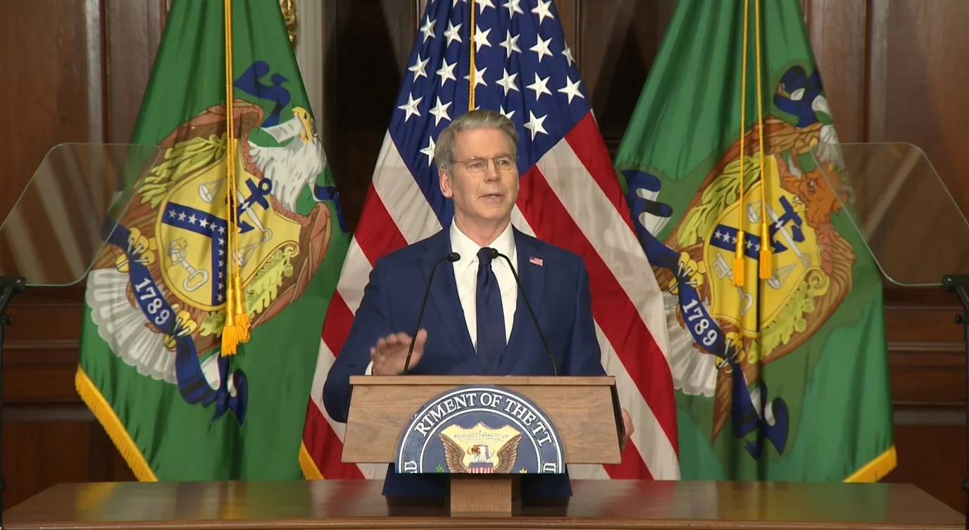 Scott Bessent speaks at a podium in the US Department of the Treasury, in front of the American flag and institutional flags.