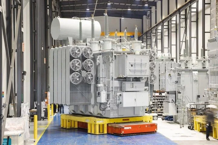 Grande transformador de potência em uma linha de produção industrial. A expansão de data centers e infraestrutura de IA está elevando a demanda por equipamentos elétricos de alta capacidade.